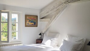 A bedroom with two beds, a window, a painting, and a radiator.