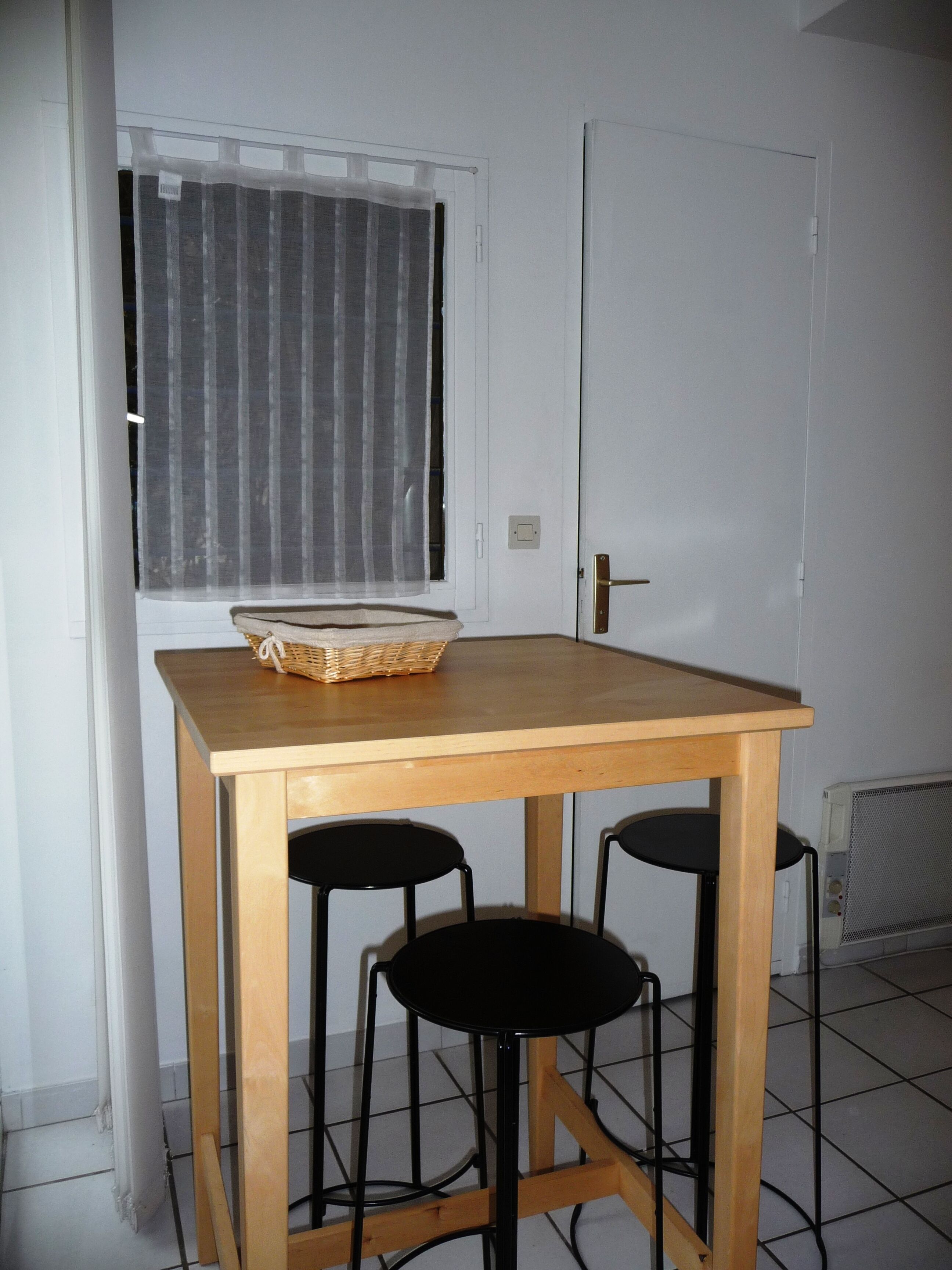 A small room with a wooden table and two black stools. A basket is placed on the table.