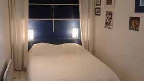 A bedroom with a bed, a window with curtains, and wall-mounted lights. - Villa 75m² classified 2*, close to shops equipped with mosquito repellent (Sanary-sur-Mer)