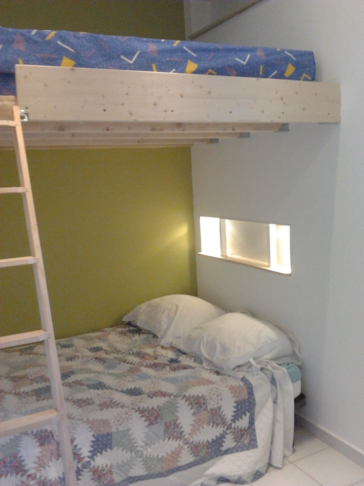 Un lit superposé avec une échelle, une couvre-lit matelassée et une table de chevet avec une lampe.