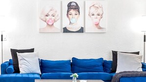 Una habitación con un sofá azul, cojines blancos y negros, y una obra enmarcada sobre el sofá.