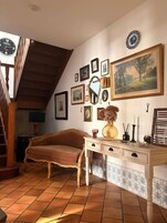 A cozy room with a wooden staircase, a brown sofa, a desk with drawers, and various framed pictures on the wall.