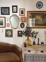 A room with a brown leather sofa, a white dresser with patterned tiles, and various framed artworks and decorative items on the walls.