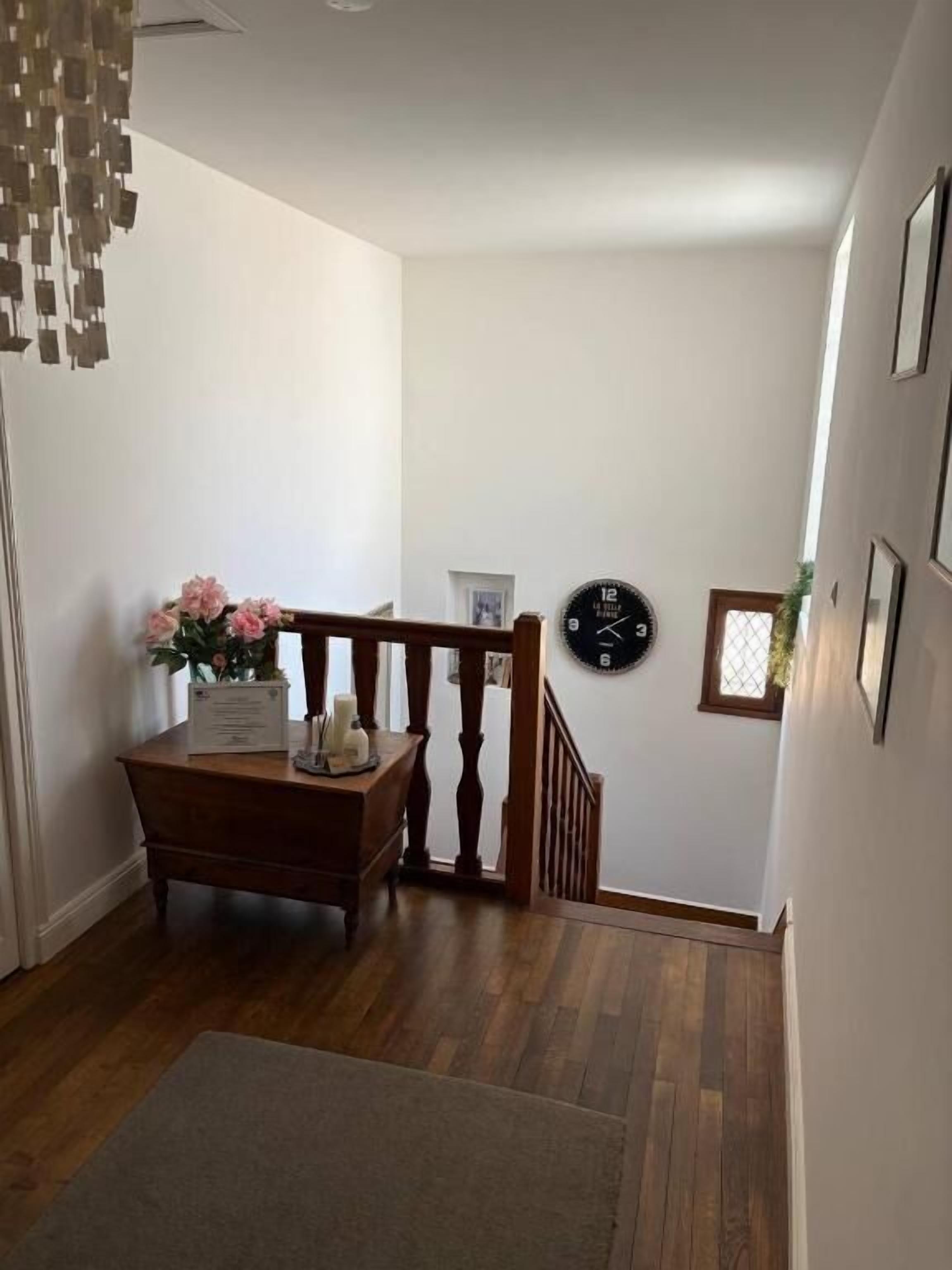 A staircase with a wooden railing, a clock on the wall, and a vase of flowers on a table.
