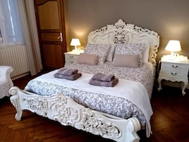 A bedroom with a large ornate bed, two bedside tables with lamps, and a wooden wardrobe.