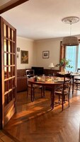 A dining area with a wooden table and chairs, a television, and a vase with flowers.