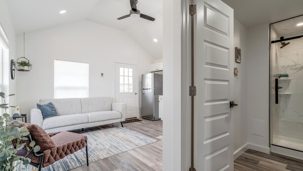 A spacious living room with a white sofa, a brown pouf, and a ceiling fan. - Charming 1-bedroom cottage on historic Rt. 66 on the west side of Yukon. (El Reno)