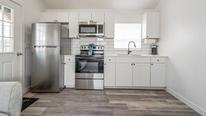 A modern kitchen with white cabinets, stainless steel appliances, and a herringbone-patterned floor. - Charming 1-bedroom cottage on historic Rt. 66 on the west side of Yukon. (El Reno)