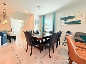 Un espace repas avec une table et des chaises en bois foncé, un coin cuisine avec un comptoir et des tabourets, et un coin salon avec un canapé et un tableau au mur.