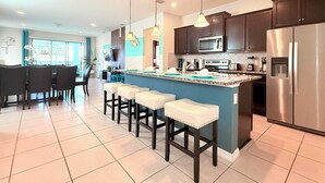 A modern kitchen with a central island, bar stools, stainless steel appliances, and pendant lighting.