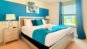 A neatly made bed with white and teal bedding, a bedside table with a lamp, and a window with curtains.