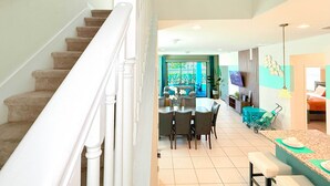 A spacious living area with a staircase, a dining table with chairs, and a kitchen area visible through an open door.