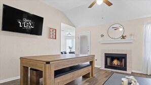 Un salon avec un banc en bois, une cheminée, un téléviseur et un ventilateur de plafond.