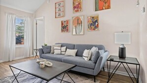 Un salon avec un canapé gris, une table basse et une lampe. Plusieurs tableaux encadrés ornent le mur.