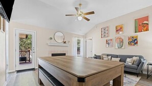Un vaste espace de vie comprenant une table à manger en bois, un canapé gris et un ventilateur de plafond.
