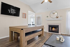 A living room with a wooden bench, a fireplace, a television, and a ceiling fan. - Hill Country Getaway | Games, Fire Pit & Deck (Leander)