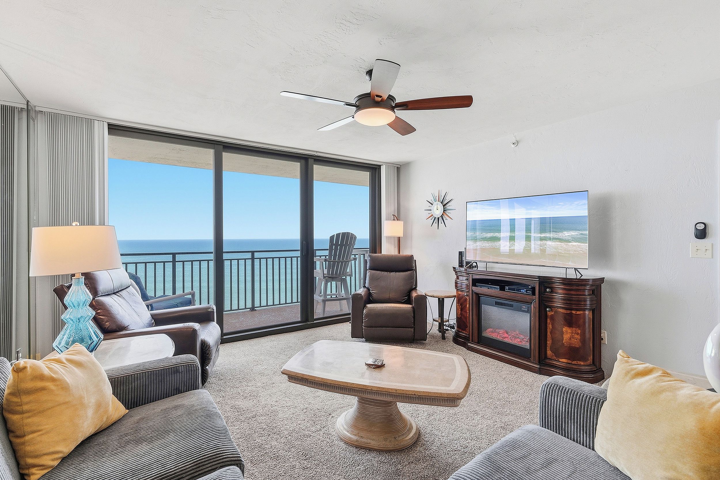 A hotel room with a balcony, a ceiling fan, a television, and a fireplace.