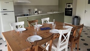 Une cuisine moderne avec une table à manger en bois, préparée pour accueillir six personnes, et dotée de chaises blanches.