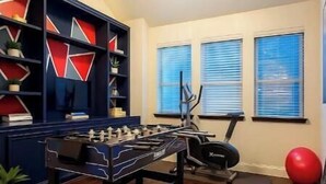 Una habitació amb taula de futbolí, equipament esportiu i una estanteria.