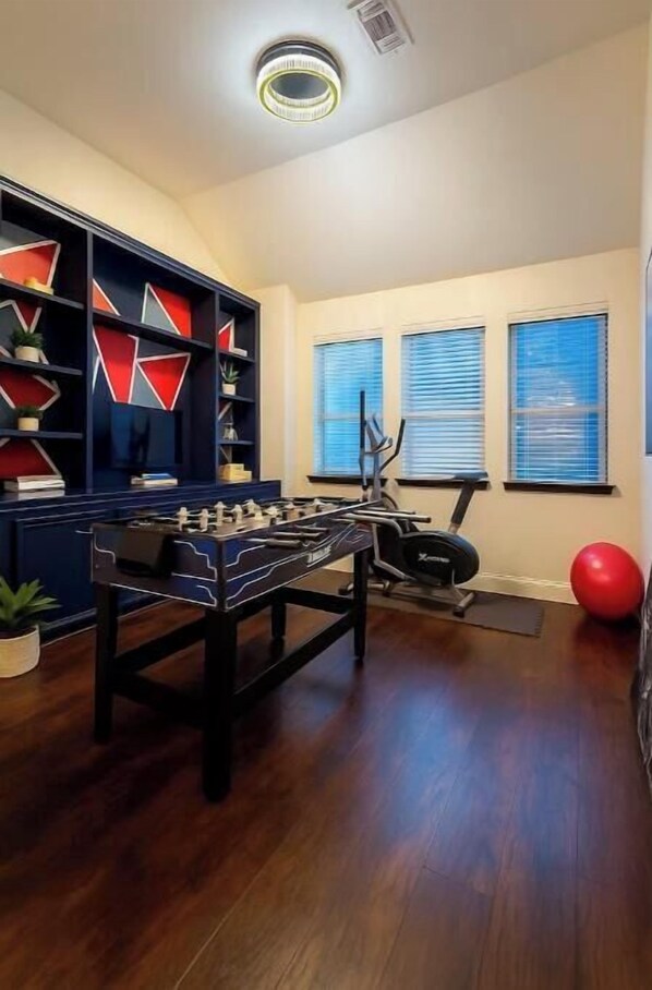 A room with a foosball table, exercise equipment, and a bookshelf.