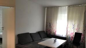 A modern living room with a dark grey sofa, a small white table, and a black chair. - 2 bedrooms in Breuberg Odenwald (Breuberg)