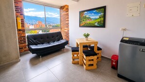Een gezellig, ruimtelijk interieur met een leren bank, een houten tafel met een plant, een koelkast en een stadsgezicht door een groot raam.