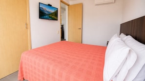 A hotel room with a bed, a television mounted on the wall, and a door leading to a bathroom.