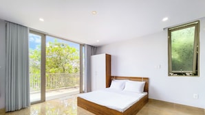 A modern bedroom with a wooden bed, large sliding glass doors, and a view of greenery outside. - Lumiere Villa Swanbay  (Nhon Trach)