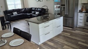 A modern kitchen with a central island, white cabinetry, and a stainless steel refrigerator. - A place to call home. (Foley)