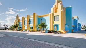 A hotel with a modern architectural design, featuring a prominent entrance with a blue and yellow facade, palm trees, and a clear sky.