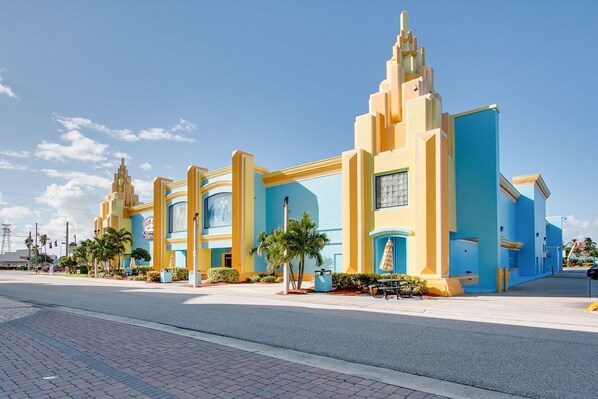 A hotel with a modern architectural design, featuring a prominent entrance with a blue and yellow facade, palm trees, and a clear sky. - Penguins on the Beach Villas (Cocoa Beach)