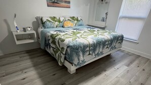 A bedroom with a bed, a nightstand, a ceiling fan, a window with blinds, and a painting on the wall.