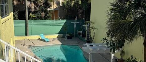 A swimming pool with a white fence, surrounded by palm trees and a green fence.