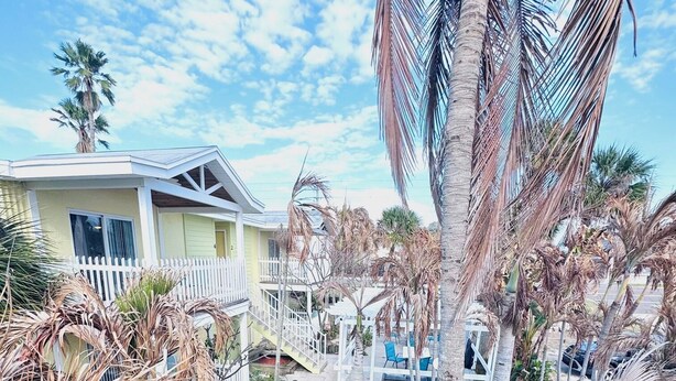 A residential area with a pathway, palm trees, and a house with a white fence.