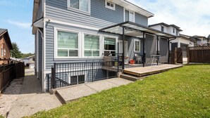 A two-story residential house with a covered patio, a fenced yard, and a clear sky. - Luxury 2 Bedroom Surrey Basement Suite, Sleeps 6 (Surrey)
