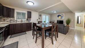 A modern kitchen with dark wood cabinets, a central island, and a dining area with a large table and chairs. - Luxury 2 Bedroom Surrey Basement Suite, Sleeps 6 (Surrey)