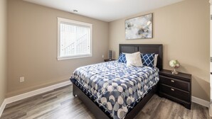 A bedroom with a bed, a nightstand, a globe, and a window with blinds. - Luxury 2 Bedroom Surrey Basement Suite, Sleeps 6 (Surrey)