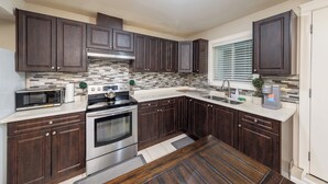 A modern kitchen with dark wood cabinets, stainless steel appliances, and a tiled backsplash. - Luxury 2 Bedroom Surrey Basement Suite, Sleeps 6 (Surrey)
