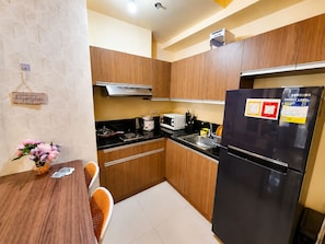 A compact kitchen with wooden cabinets, a black refrigerator, a microwave, and a stove. - Levi & Moon Relax and Chill (Pasay)