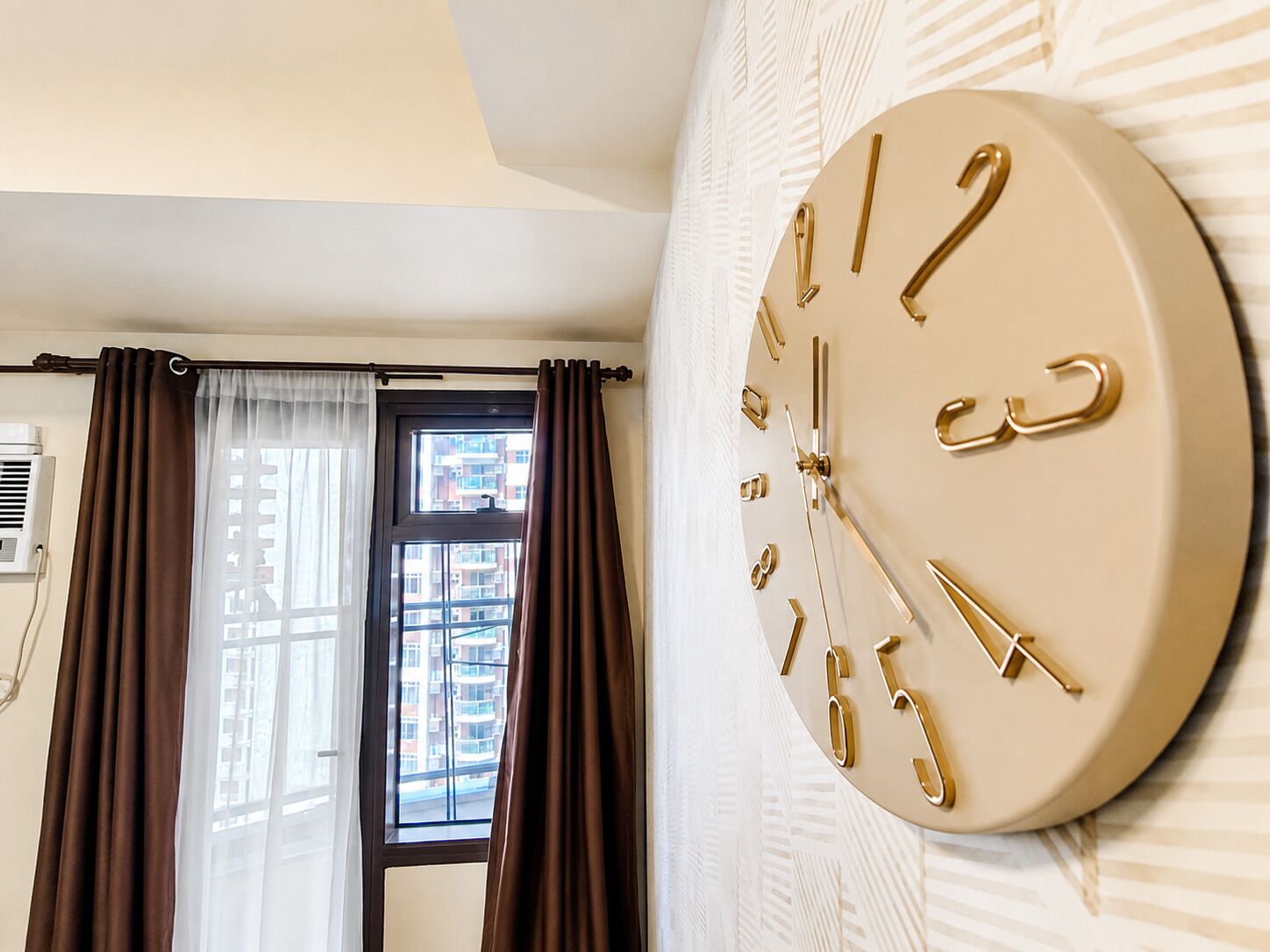 A room with a large wall-mounted clock, a window with curtains, and an air conditioning unit.