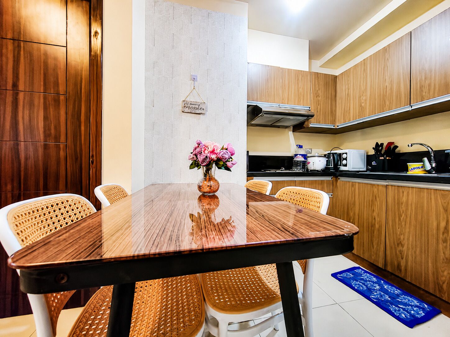 A modern kitchen with wooden cabinets, a stainless steel range hood, and a dining area with a wooden table and woven chairs.