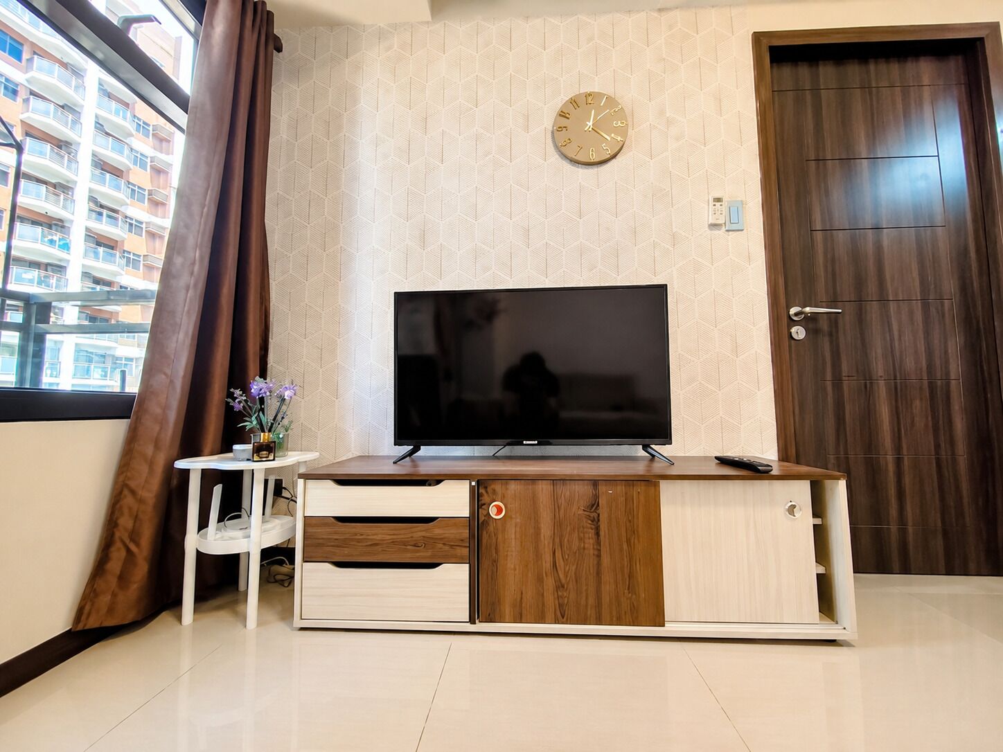 Un salon moderne avec un téléviseur à écran plat posé sur un meuble en bois, une horloge au mur et une porte sur le côté droit.