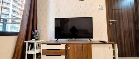 A modern living room with a flat-screen TV on a wooden cabinet, a clock on the wall, and a door to the right.
