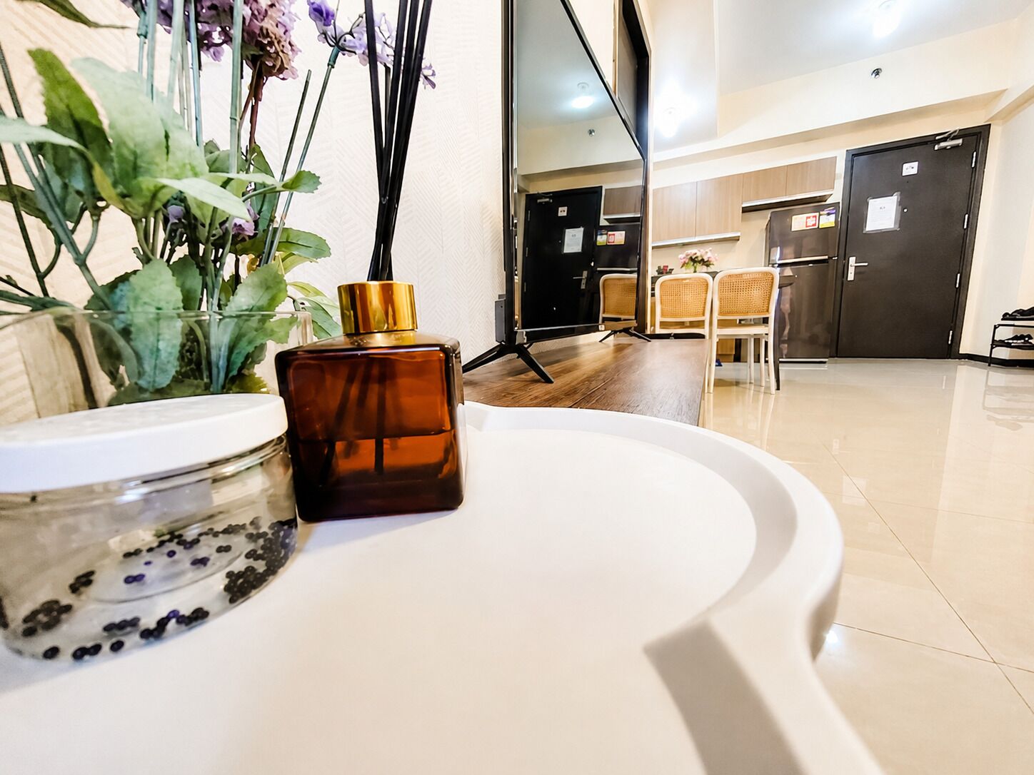 Un baño moderno con un lavamanos blanco, un frasco de vidrio con cuentas negras y una botella marrón.