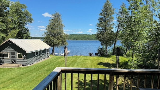 A cabin with a deck overlooking a lake, surrounded by trees. - Charming 2-bedroom cabin in Portage Lake (Portage Lake)