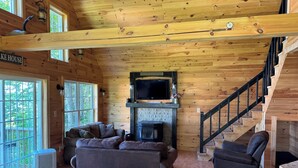 A cabin interior with a fireplace, a sofa, a television, and a staircase. - Charming 2-bedroom cabin in Portage Lake (Portage Lake)