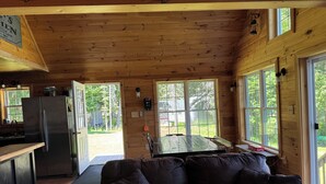 A cozy cabin interior with a wooden ceiling, a dining table, a sofa, and a kitchen area with a refrigerator. - Charming 2-bedroom cabin in Portage Lake (Portage Lake)