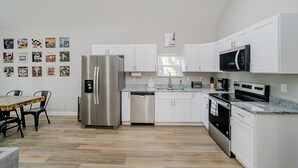 A modern kitchen with white cabinets, stainless steel appliances, and a dining area with a wooden table and chairs. - BRAND NEW Spacious and Uniquely Musical Home near Downtown Indianapolis! (Indianapolis)