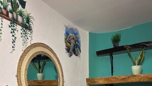 A bathroom with a wooden vanity, a round mirror, a sink with a marble-like backsplash, and shelves with plants and a swan decoration.