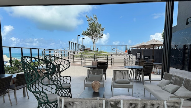En udendørs siddeplads med fletmøbler, udsigt til havet og en trappe op til en etage over.